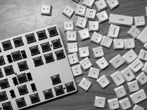Teclado mecânico desmontado sobre a mesa, em preto e branco